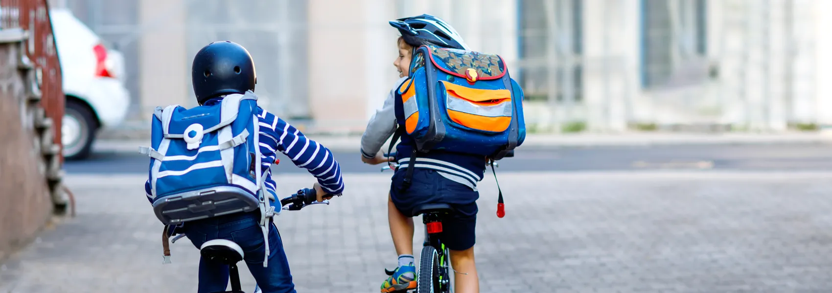 Två små skolpojkar cyklar tillsammans, med ryggsäckar och cykelhjälmar.