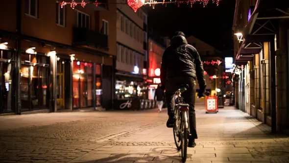 Man som cyklar inne i en stad en sen kväll.